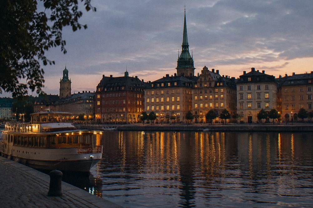 Stockholm's Old Town seen across the water at dusk, with warmly lit historic buildings reflected in the calm harbor