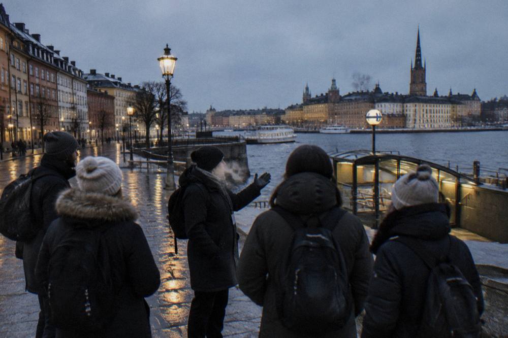 A guide talking to a small group of winter visitors in a lamplit Old Town alley in Stockholm