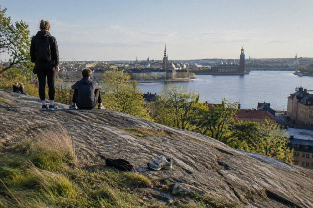 Walkers on a cliffside path above Stockholm with water and rooftops below