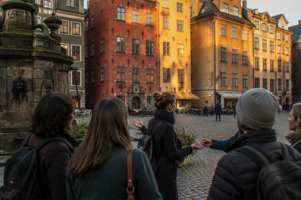A local guide speaking to a small group of visitors gathered on a cobblestone square in Stockholm's Old Town