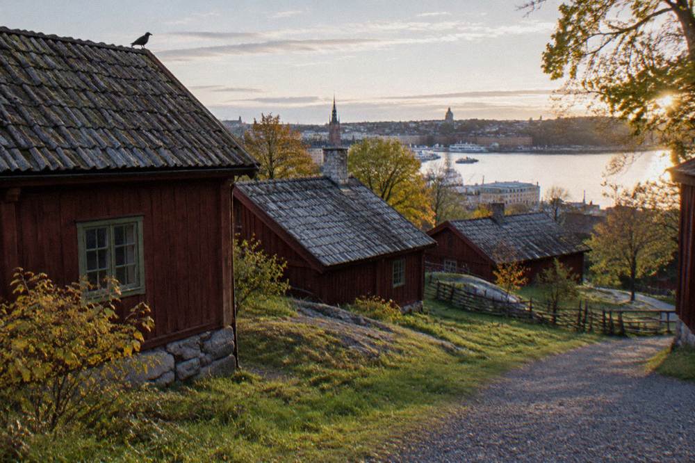 Wooden historic buildings on a hillside at Skansen with Stockholm harbor in the distance