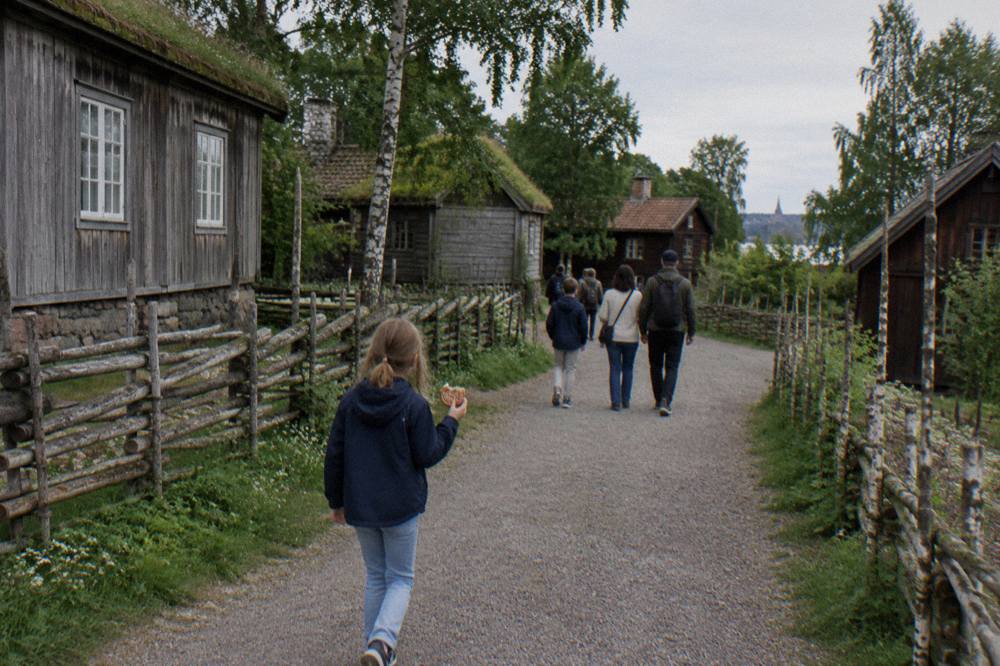 Visitors walking a gravel path between historic farmhouses at the Skansen open-air museum
