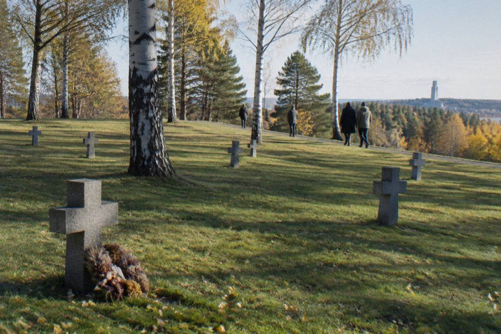 Visitors walking between granite crosses and birch trees along a wide grassy ridge at Skogskyrkogarden