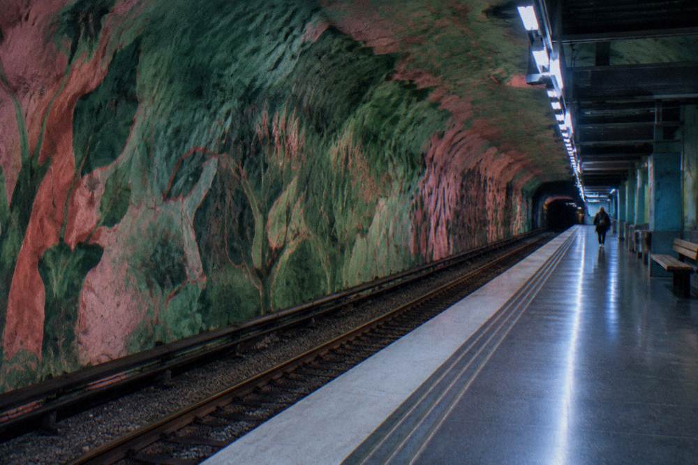A colorful Stockholm metro platform with sculpted rock walls and artwork along the tracks