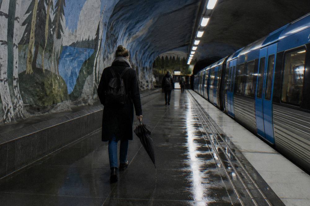 A commuter walking along a Stockholm metro platform with murals covering the rough rock wall