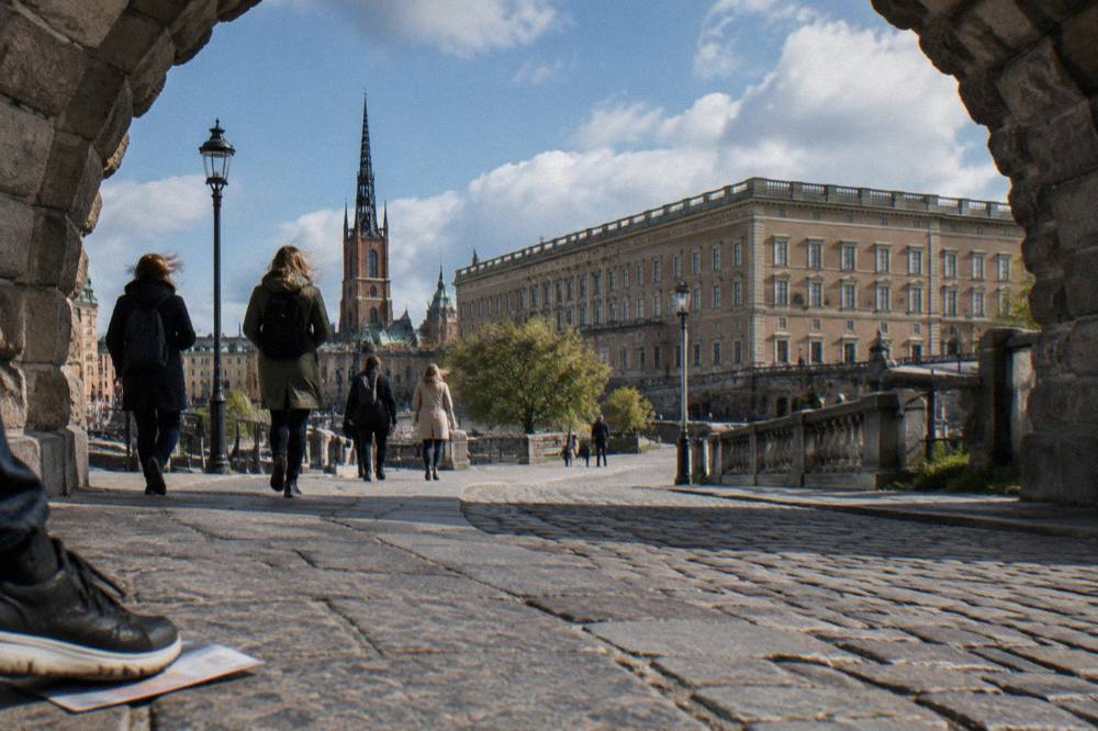 Visitors walking across a stone bridge toward the Royal Palace in Stockholm on a bright day