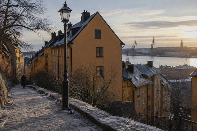 Elevated outlook over Sodermalm, Stockholm, Sweden, rooftops and chimneys stepping down toward the water, ferries crossing the channel toward the Old Town, late afternoon haze over the islands.