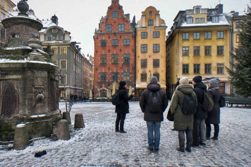 A local guide speaking to a small group of visitors in a Stockholm Old Town square lined with colourful historic buildings