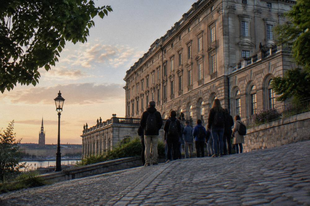 A walking tour group pausing on a cobbled lane in Stockholm's Old Town with the Royal Palace visible in the background