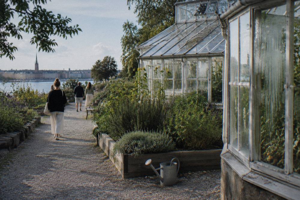 Visitors strolling a garden path beside old glasshouses at Rosendals Tradgard on a mild afternoon