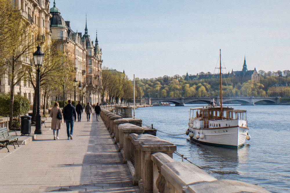 A stone quay in central Stockholm with a bridge connecting two islands and people walking