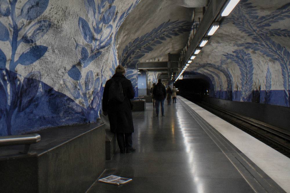 A blue-line metro platform in Stockholm with colourful artwork along the walls and travellers waiting