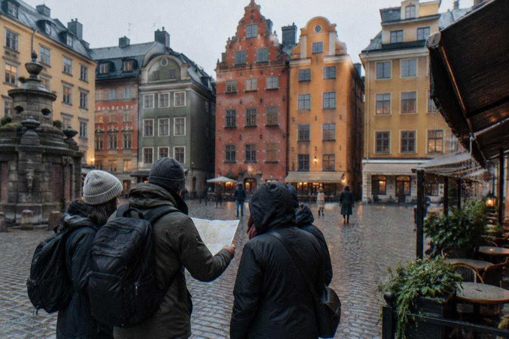 A guide holding up a printed map while speaking to a small group gathered on a cobbled Stockholm square