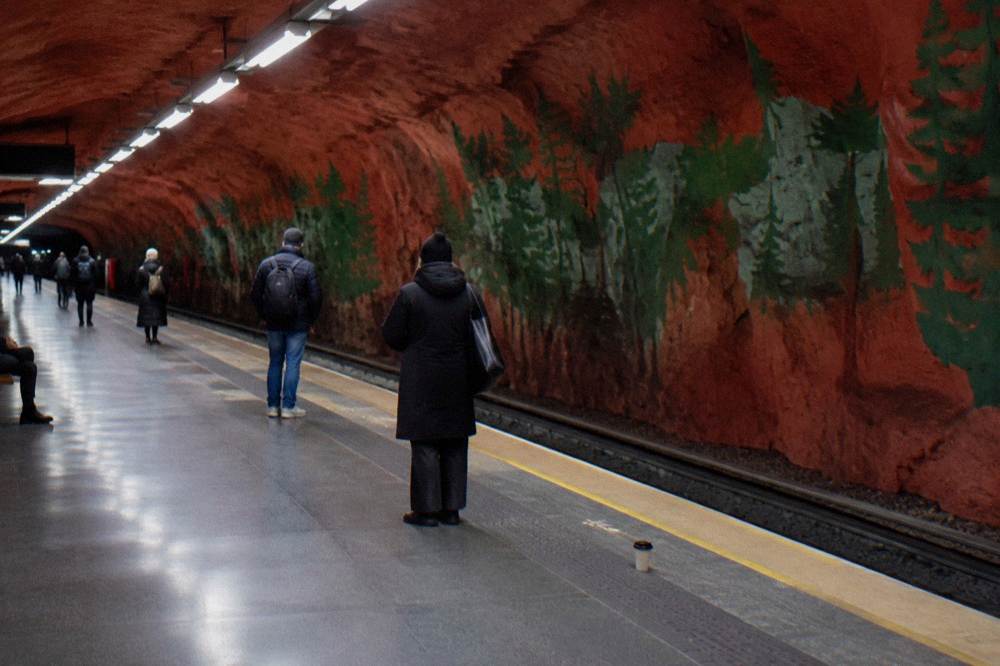 A Stockholm metro platform with colorful artwork along the walls and travelers waiting for a train