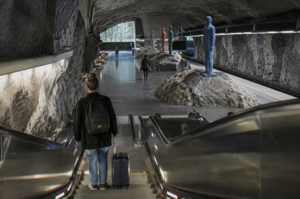 A traveler on a Stockholm metro escalator descending toward a platform with sculptural artwork overhead